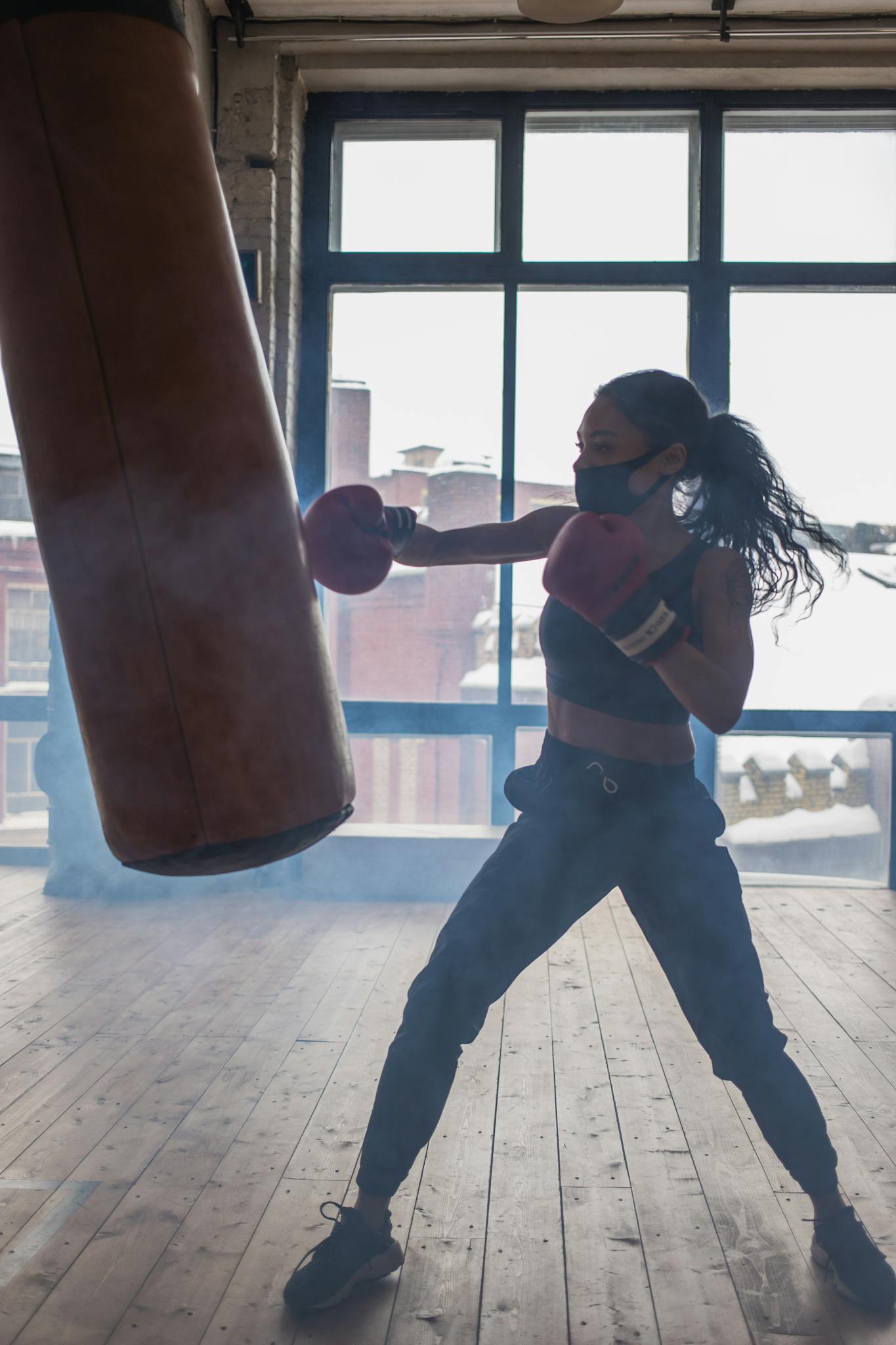 Active black boxer punching heavy bag while exercising in gymnasium